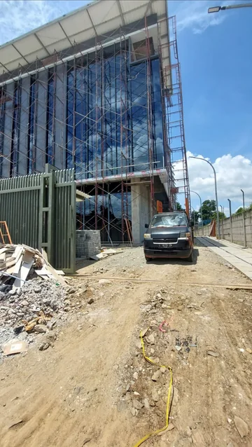Fasad bangunan bertingkat dengan perancah terpasang dan lahan proyek di depannya